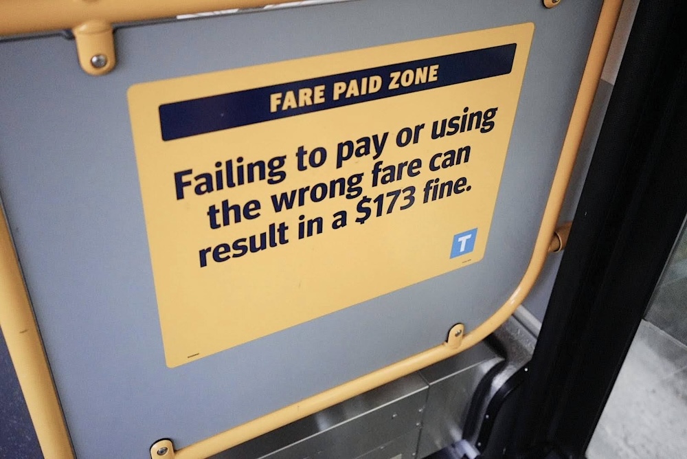 A yellow sign on the back of a grey seat on public transit says, &lsquo;Fare paid zone: Failing to pay or using the wrong fare can result in a $173 fine.&rsquo;