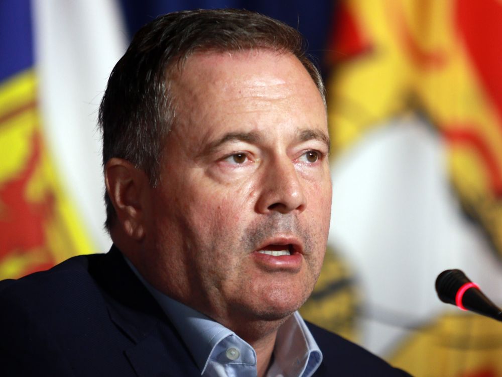 A closeup photo of a man in his mid-50s with light-toned skin and short dark hair speaks at a microphone.
