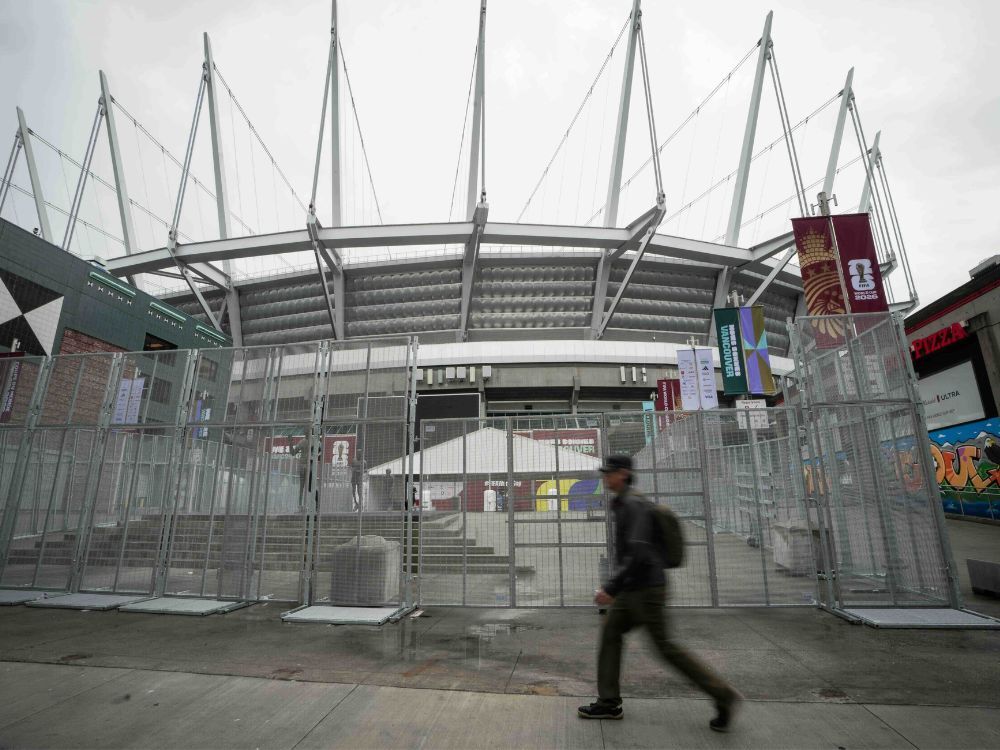 A person walks past chain link fencing with BC Place in the background.