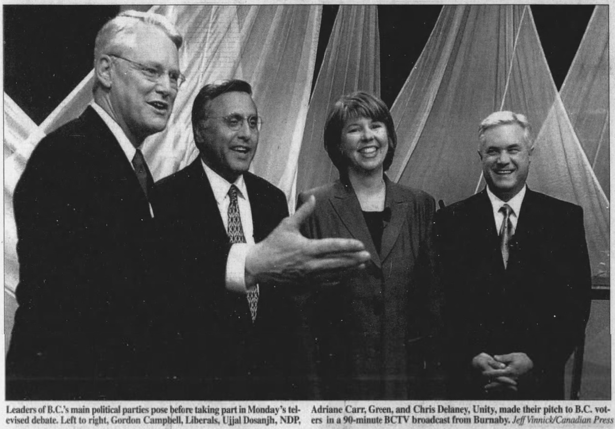 A black and white photo shows three men and a woman smiling on a debate stage.