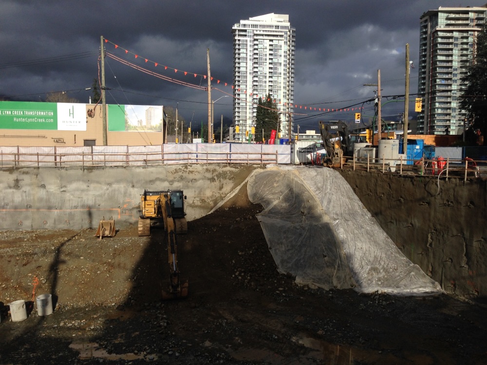 A large hole in the ground with a condo tower rising behind it catching the light.