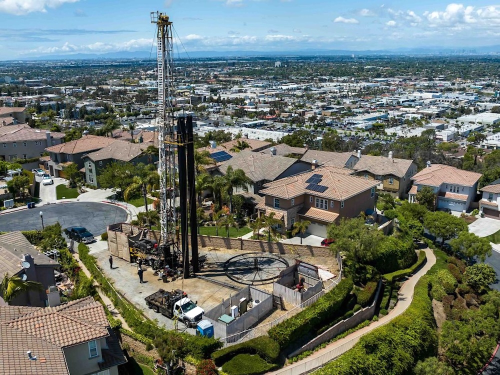 A very tall white oil well rises on a lot in the middle of a California suburb.