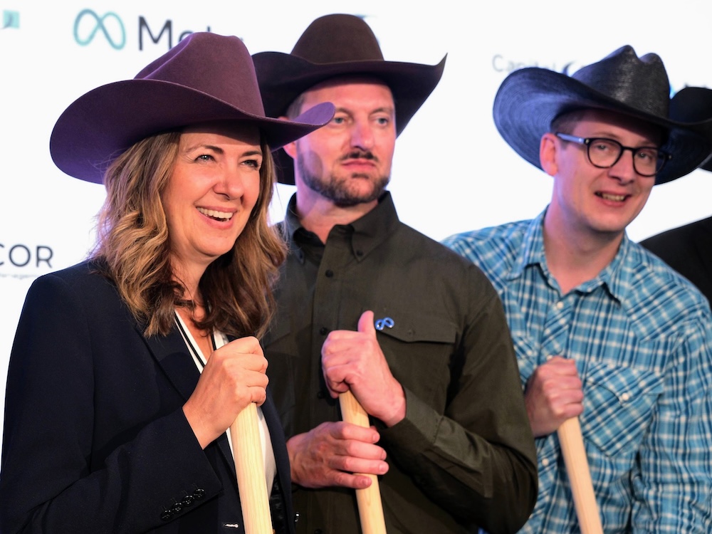 Danielle Smith and two middle-aged light-skinned men pose holding  shovels. They are wearing cowboy hats.