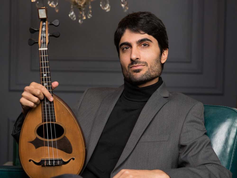A man holding an aud looks down on the strings amidst a dark, smoky backdrop.

