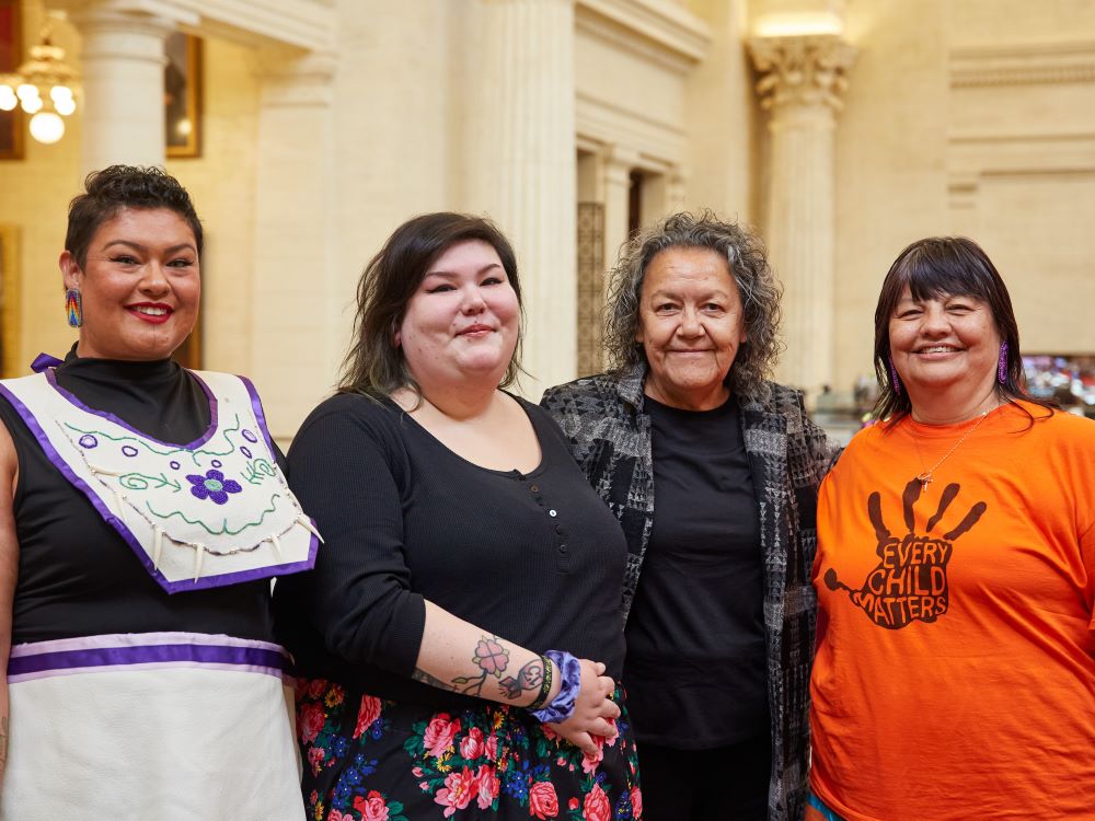 Four people smile for the camera in a brightly lit hall with columns and high ceilings. 