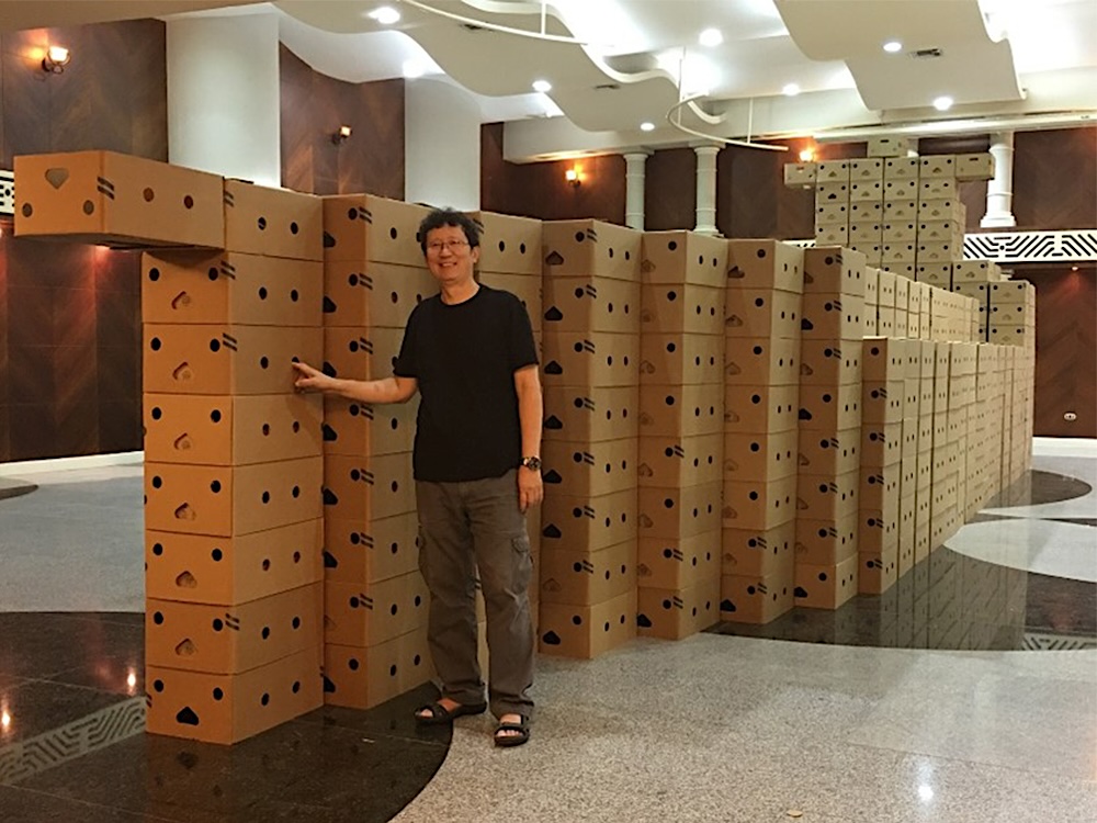 Artist Gu Xiong posing in front of his 2016 installation &lsquo;Yellow Cargo&rsquo; at Machala Sal&oacute;n, Ecuador. The installation is made of cardboard boxes and represents a cargo ship.