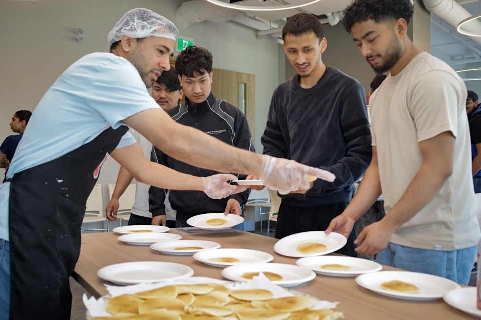 A man wearing an apron and hairnet serves pancakes.