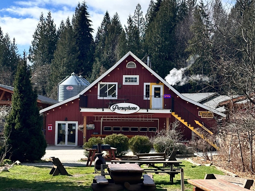 The frontage of Persephone Brewing Co. in Gibsons, B.C., features a burgundy building with a peaked roof against a stand of tall coniferous trees.