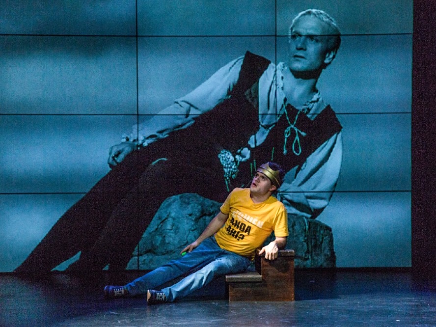 A young actor reclines in front of a picture of Sir Laurence Olivier portraying Prince Hamlet.