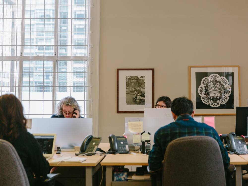 Four people at work in the Tyee office. One is talking on the phone and one is working on a laptop.