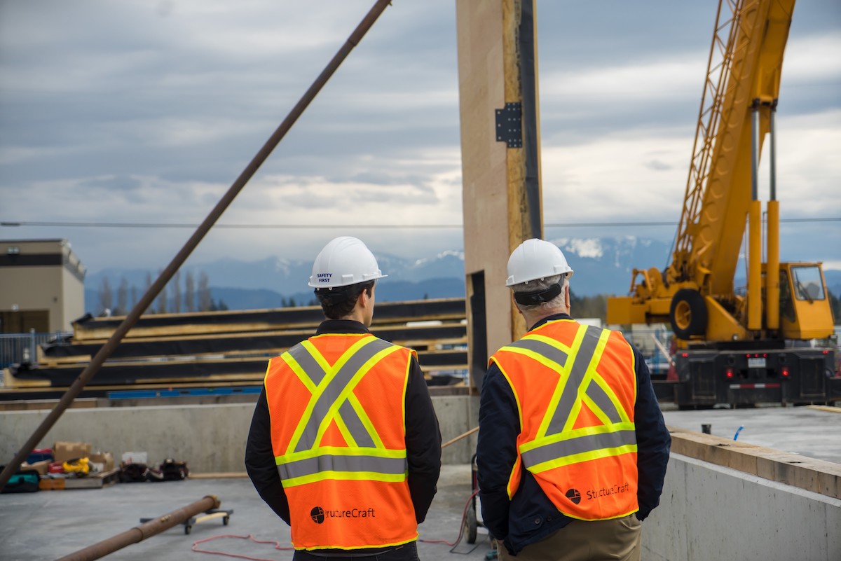 Two men in hard hats are seen from behind at a construction site.