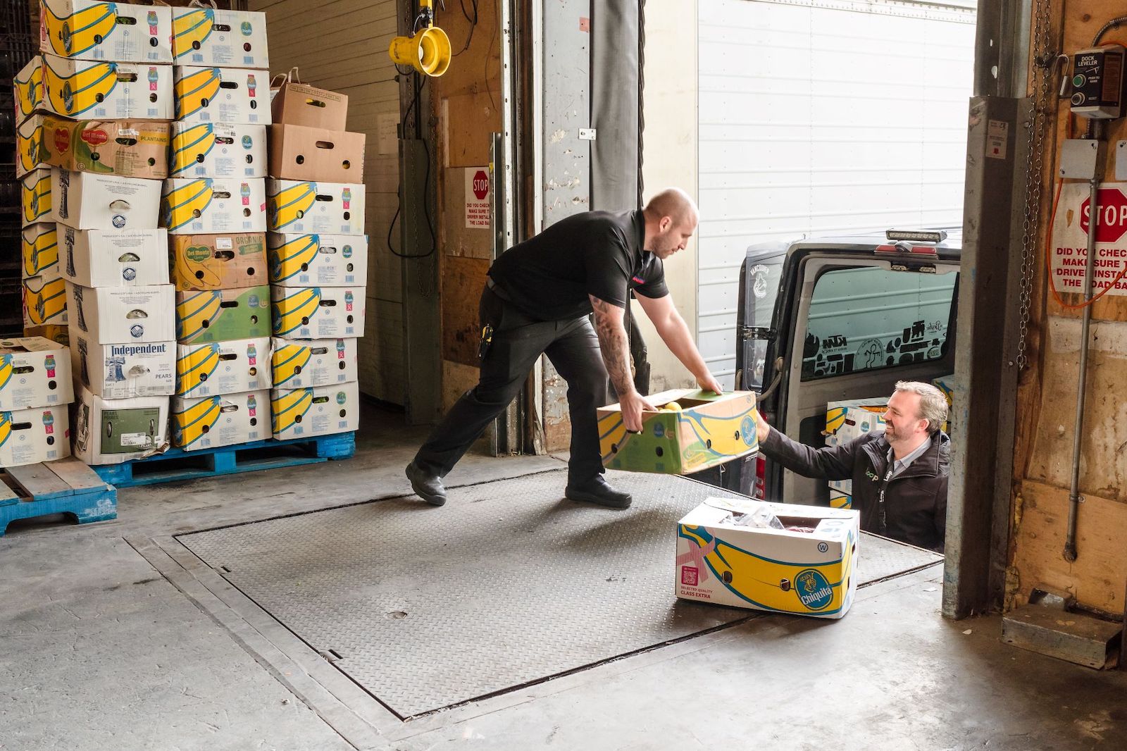 A light-skinned man dressed in a black shirt and pants loads banana boxes onto pallets.