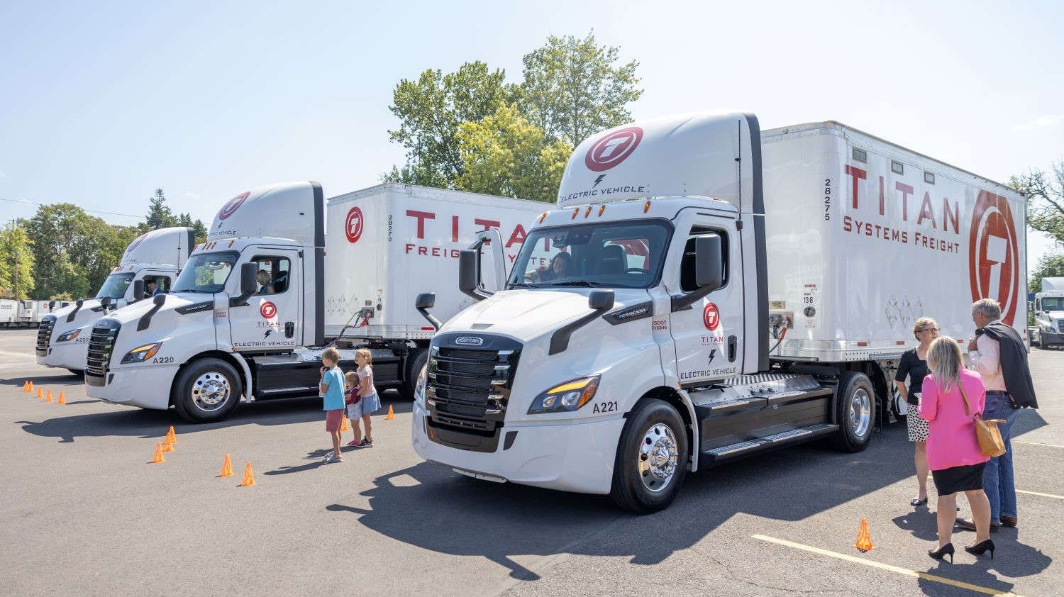 Three electric trucks in a parking lot. They are white with 'Titan Freight Systems' painted in red.