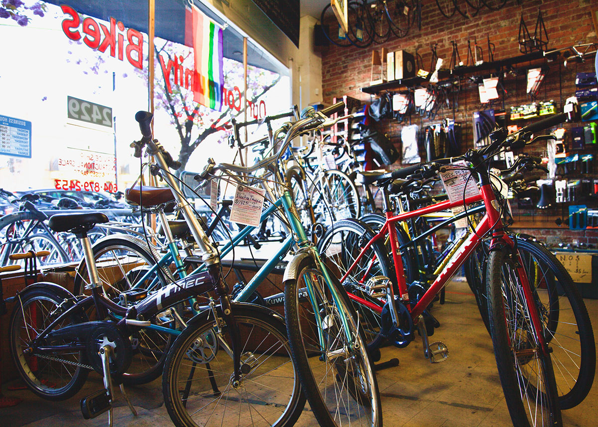About a dozen bicycles in different shapes, sizes, colours and styles are parked inside, in front of the store window. Bike accessories are mounted on the rear brick wall.