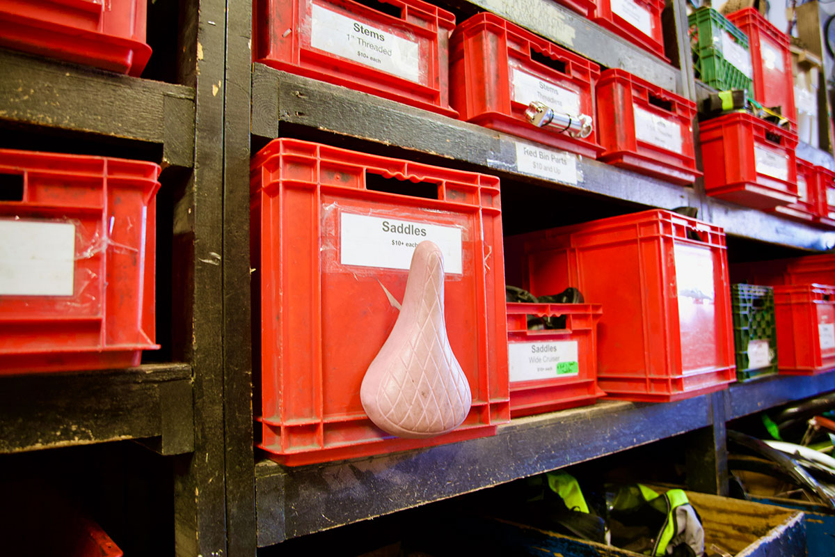 Wooden shelves painted black hold a dozen red, plastic bins of varying sizes that hold used bike parts.