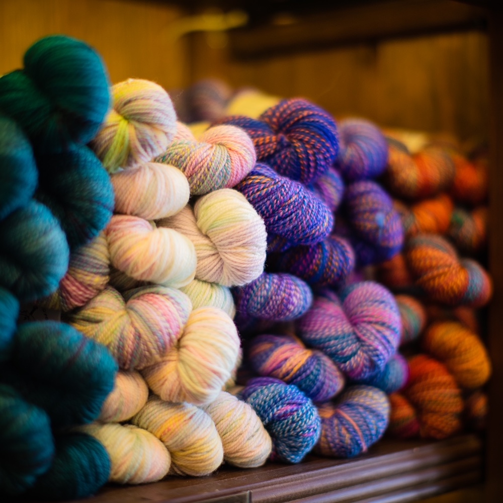 Skeins of yarn in different colourways sit on a shelf.