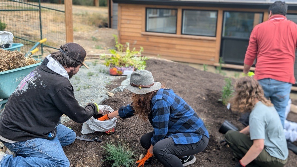 Three people seen from behind work with small plantings and soil.