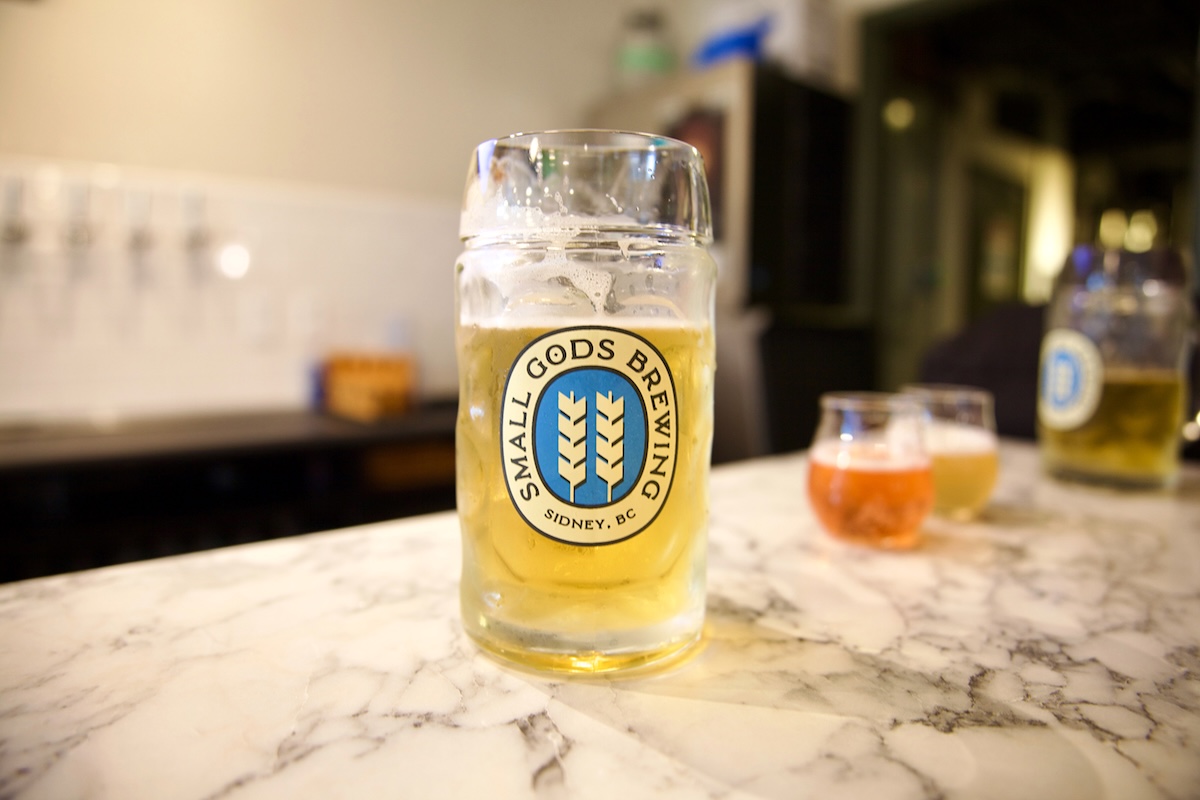 A glass stein two-thirds full of a light yellow beer sits on a marble countertop.