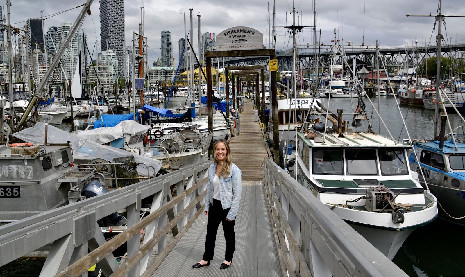 A woman with light skin and long blond hair stands on a gangway surrounded by boats at the Fishermen&rsquo;s Wharf in Vancouver&rsquo;s False Creek.