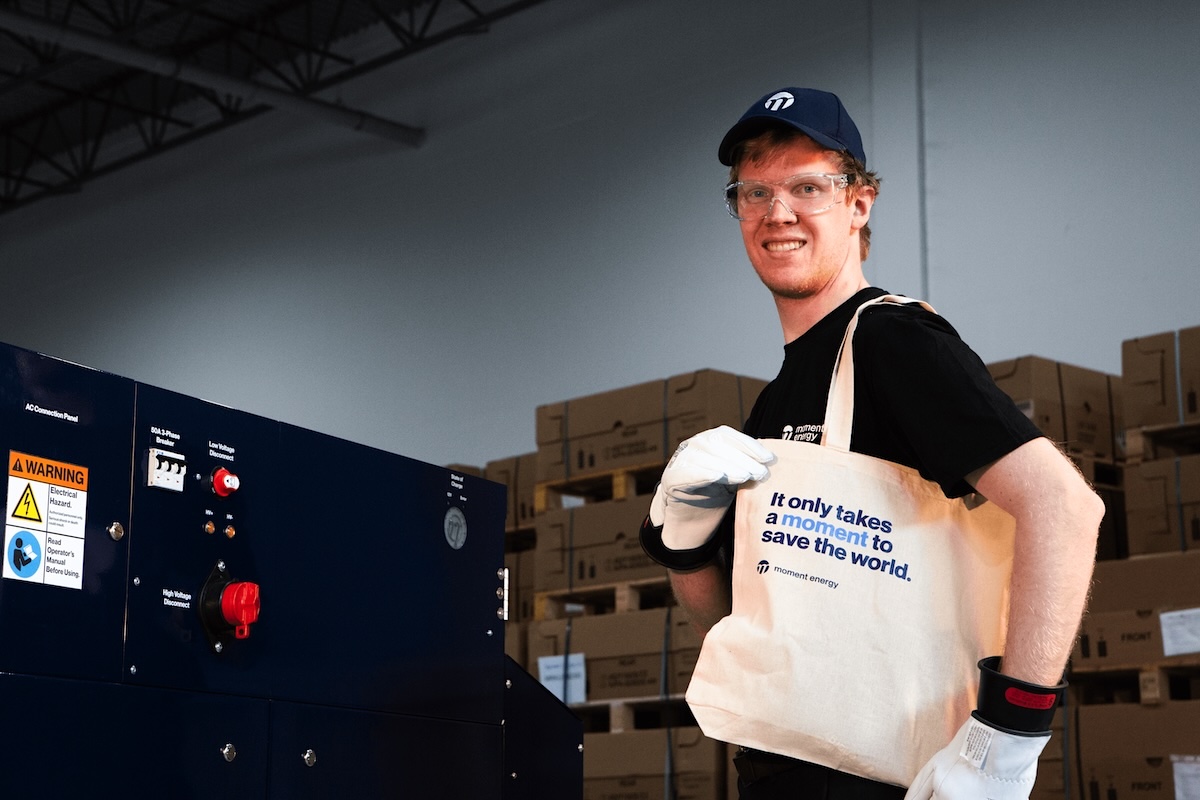 A staff member at Moment Energy inside a warehouse holds a tote bag. It reads, &lsquo;It only takes a moment to save the world.&rsquo;