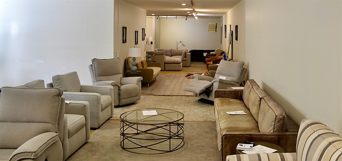 About a dozen recliners and couches rest in a long room, most in beige or soft colours. 